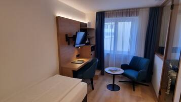 Una habitación de hotel con cama, escritorio, silla, una mesita y un sofá.
