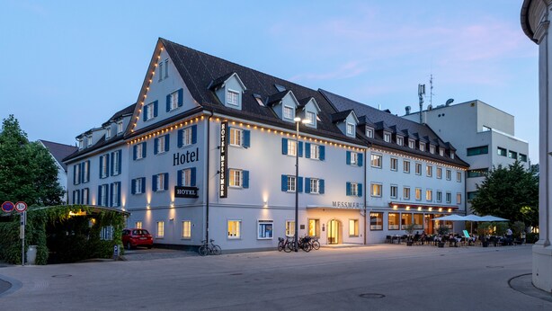 A hotel with multiple stories, a balcony, and a well-lit entrance. - Hotel Messmer (Bregenz)