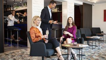 A modern bar area with a bartender, two seated guests, and a bar counter with various bottles.