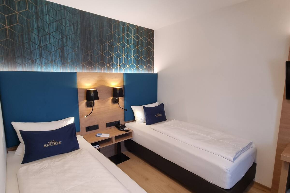 A hotel room with two single beds, a desk, and a wall-mounted TV.
