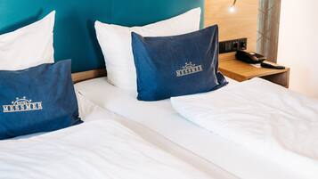 Habitación de hotel con cama, dos almohadas, mesita de noche, lámpara y pared con un diseño geométrico.