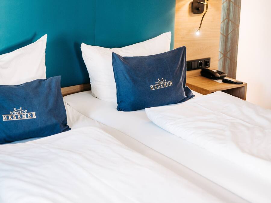 Habitación de hotel con cama, dos almohadas, mesita de noche, lámpara y pared con un diseño geométrico.