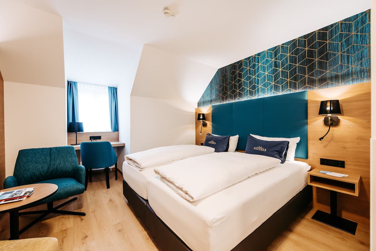 A hotel room with two beds, a desk, a chair, and a small table.
