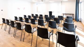 Un salón de conferencias con filas de sillas negras, una pizarra y un proyector sobre un soporte.