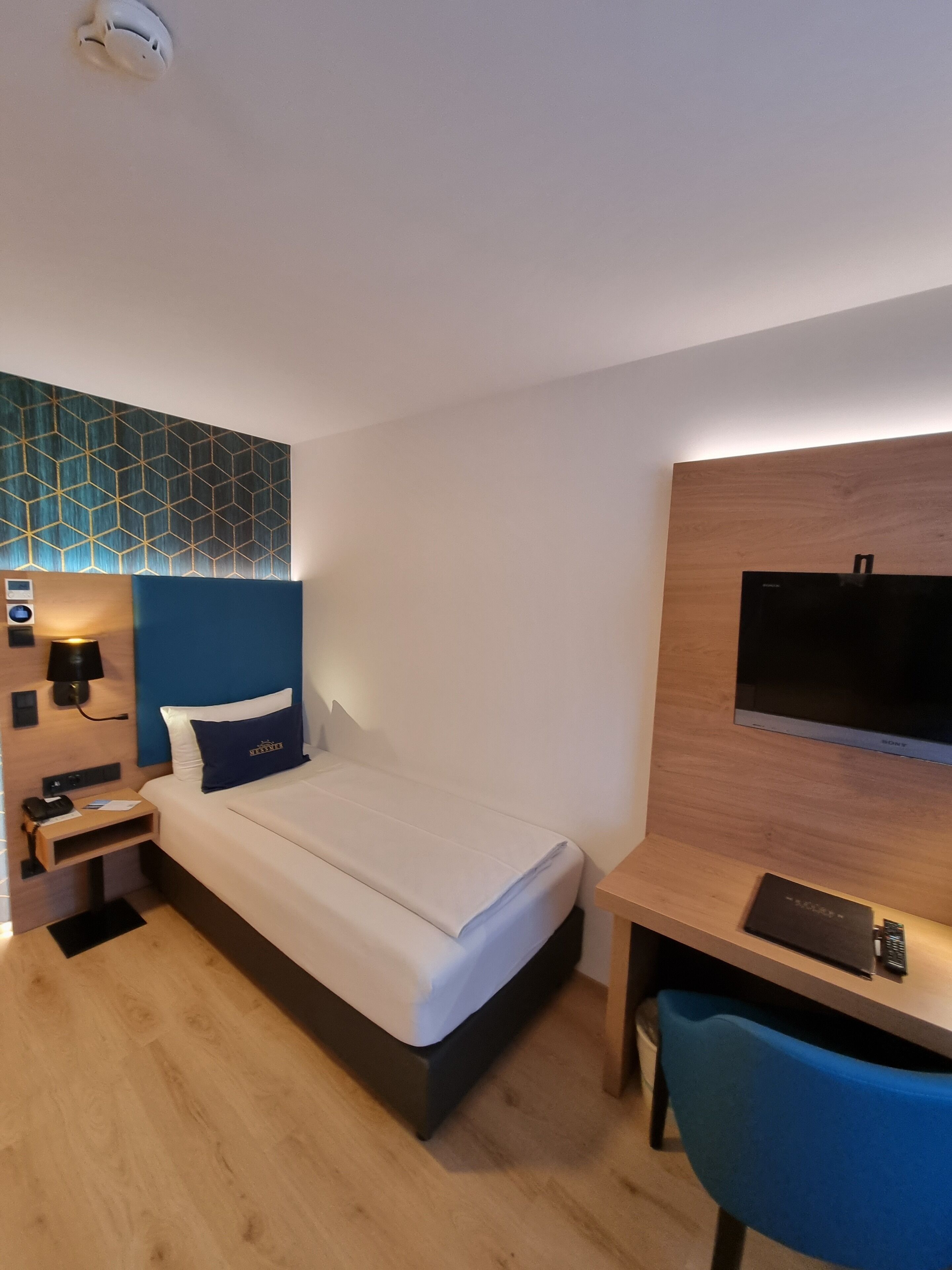 Une chambre d’hôtel comprenant un lit, une table de chevet, une lampe et un bureau avec une chaise.