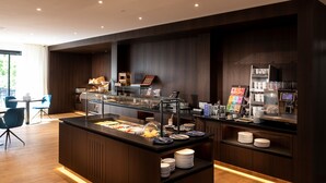 A modern breakfast bar with a variety of food options, a coffee machine, and a seating area with chairs. - Hotel Messmer (Bregenz)