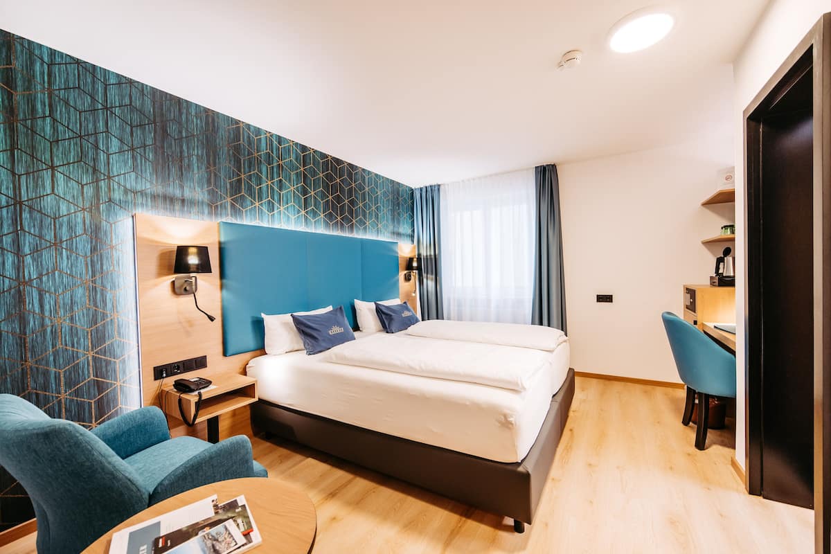 A modern hotel room with a large bed, a desk, and a chair.