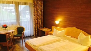 A hotel room with a wooden bed, a desk with a chair, and a window with curtains. - Hotel St. Hubertushof (Zell am See)