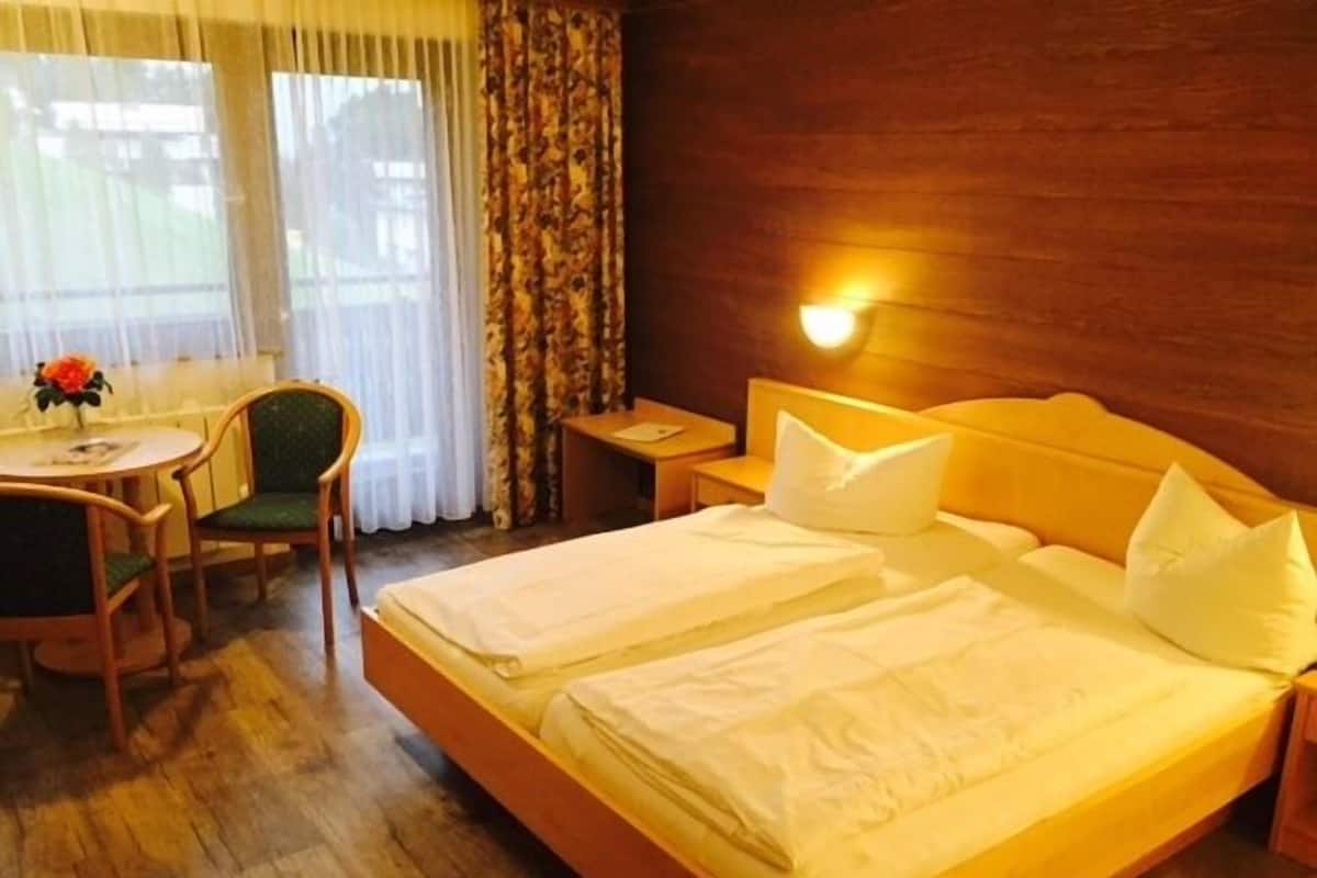 A hotel room with a wooden bed, a desk with a chair, and a window with curtains.