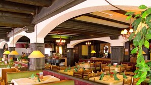 A restaurant with booths and tables, wooden beams, chandeliers, and green plants. - Hotel St. Hubertushof (Zell am See)