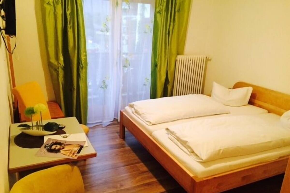 A hotel room with a wooden bed, a desk with a chair, and a window with green curtains.