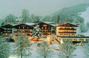 A hotel with multiple buildings, snow-covered trees, and a large tree in the foreground. - Hotel St. Hubertushof (Zell am See)