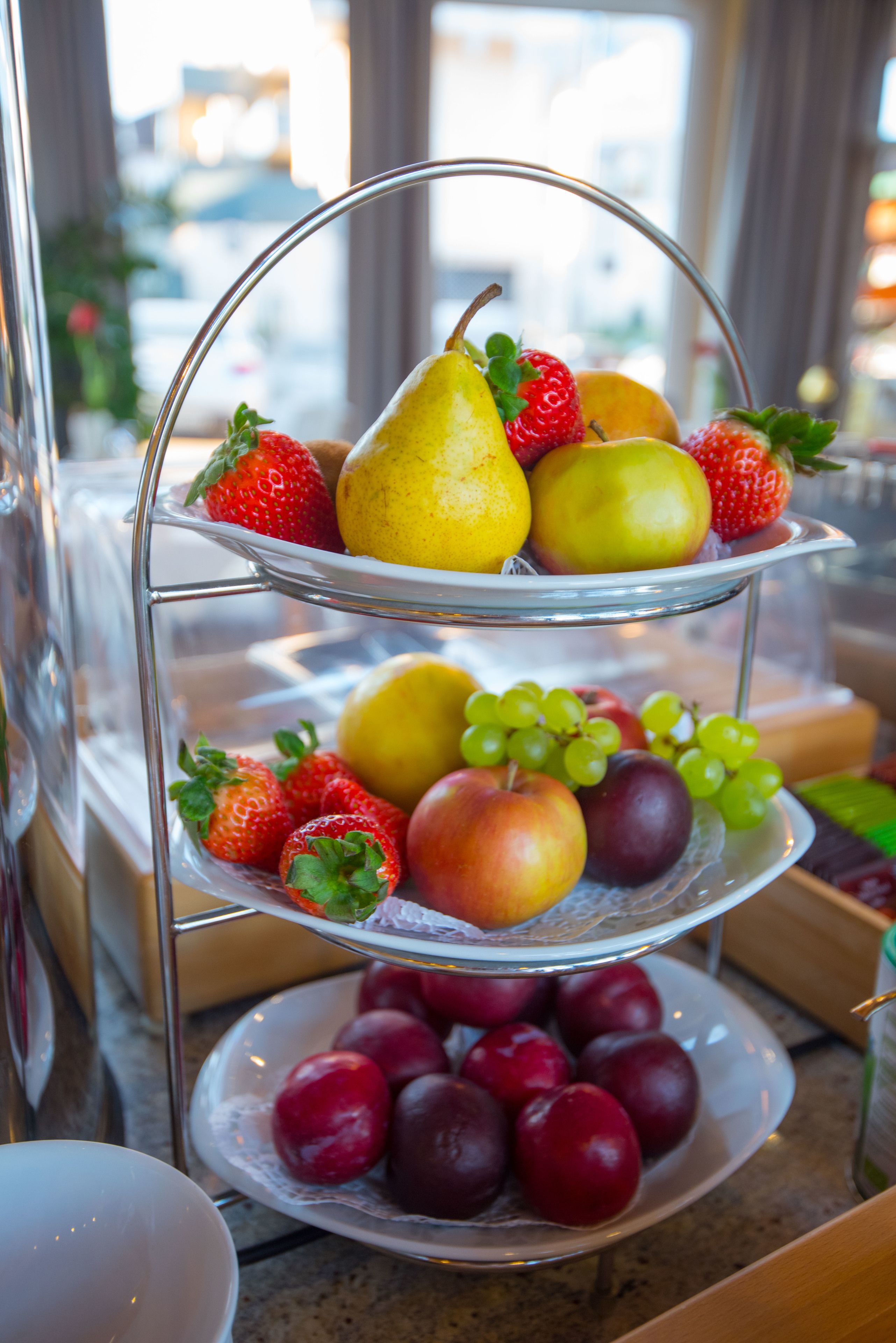 A three-tiered fruit stand with strawberries, pears, apples, and grapes.