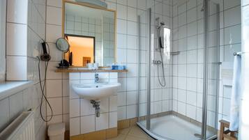 A modern bathroom with a white sink, mirror, and glass-enclosed shower.