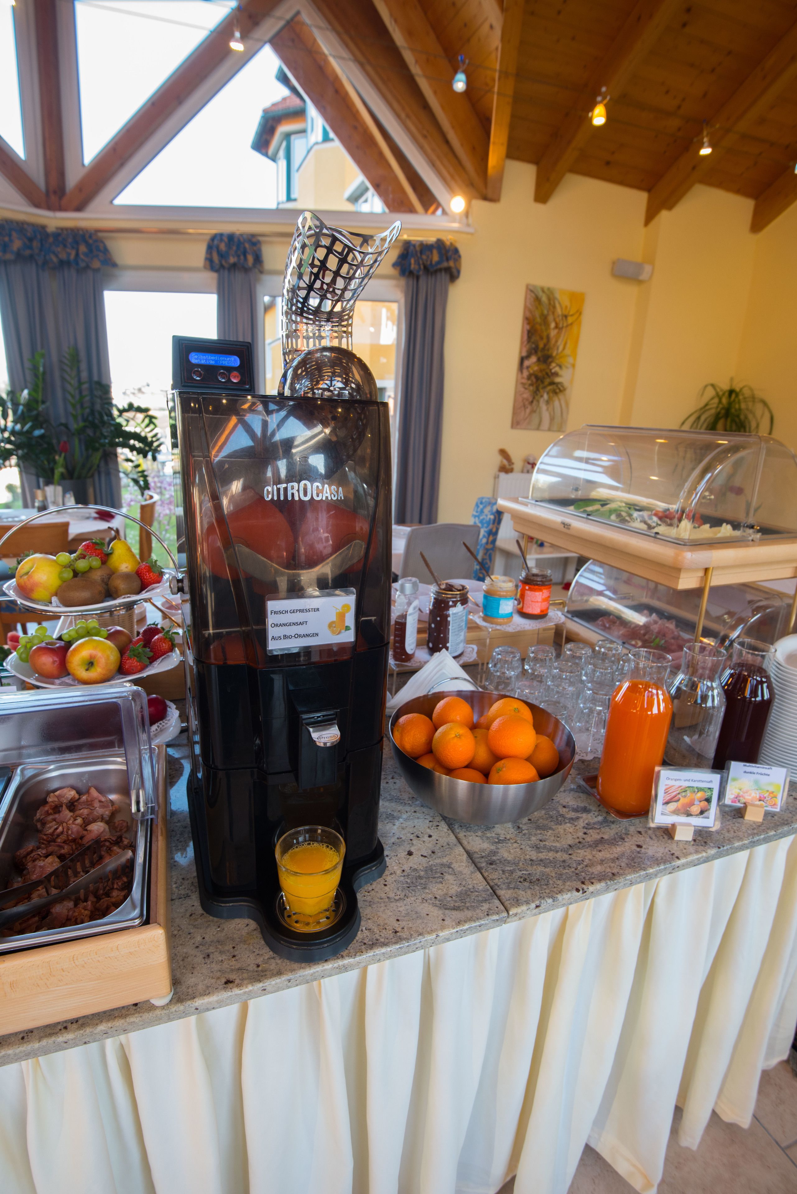 A breakfast buffet with a self-serve juice dispenser, fruit bowls, and various breakfast items.