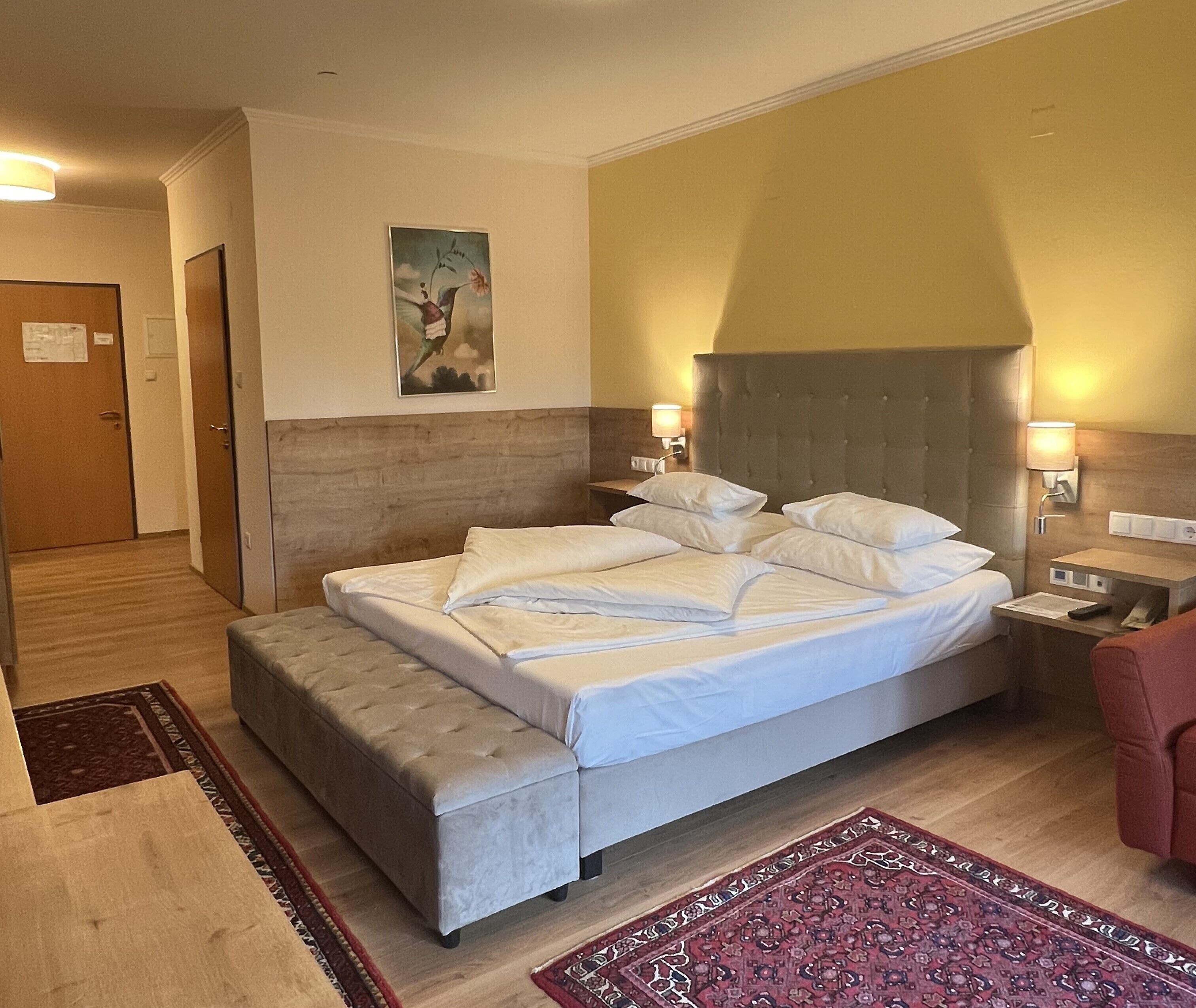 Ett hotellrum med en stor säng, en liten soffa, ett nattduksbord och en vägglampa.