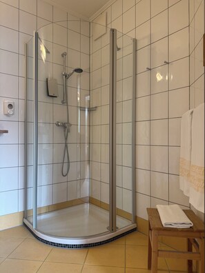 A glass-enclosed shower stall with a handheld showerhead and a wall-mounted faucet.