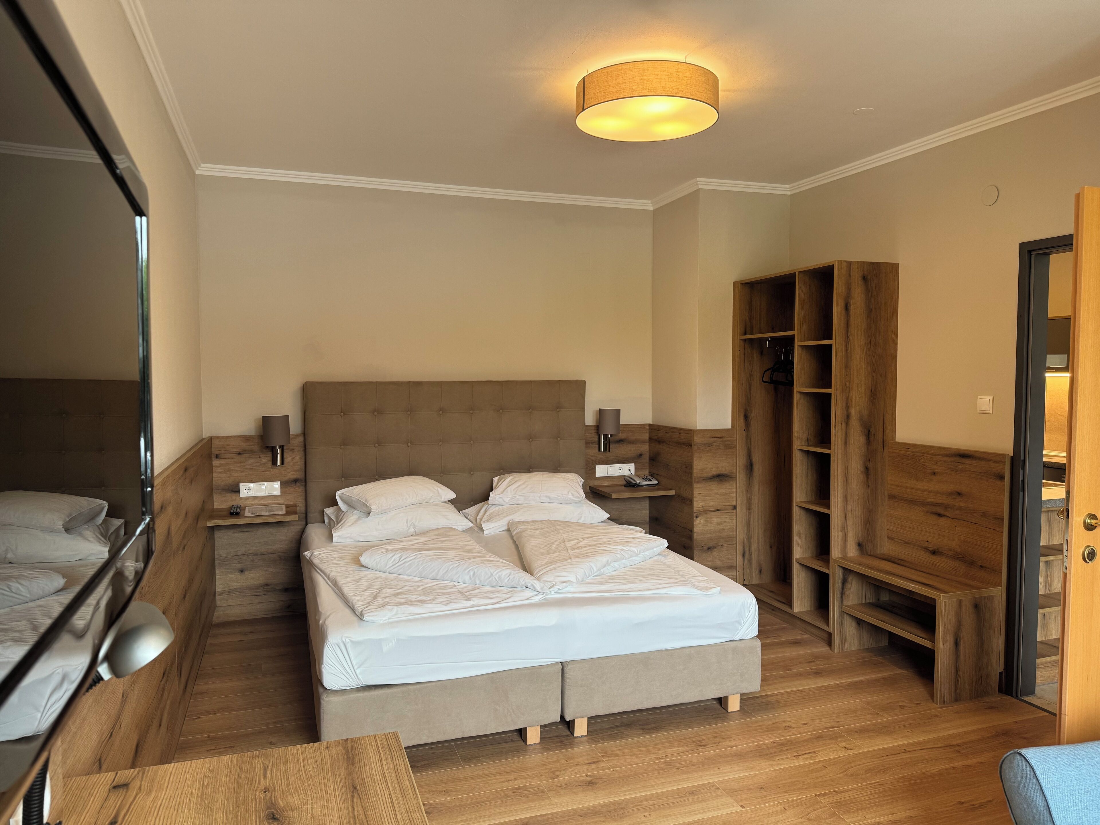 Una habitación de hotel con una cama grande, mesitas de noche, un armario de madera y un espejo.
