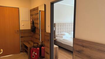 Habitación de hotel con piso de madera, una cama con ropa de cama blanca, un banco de madera y una maleta.