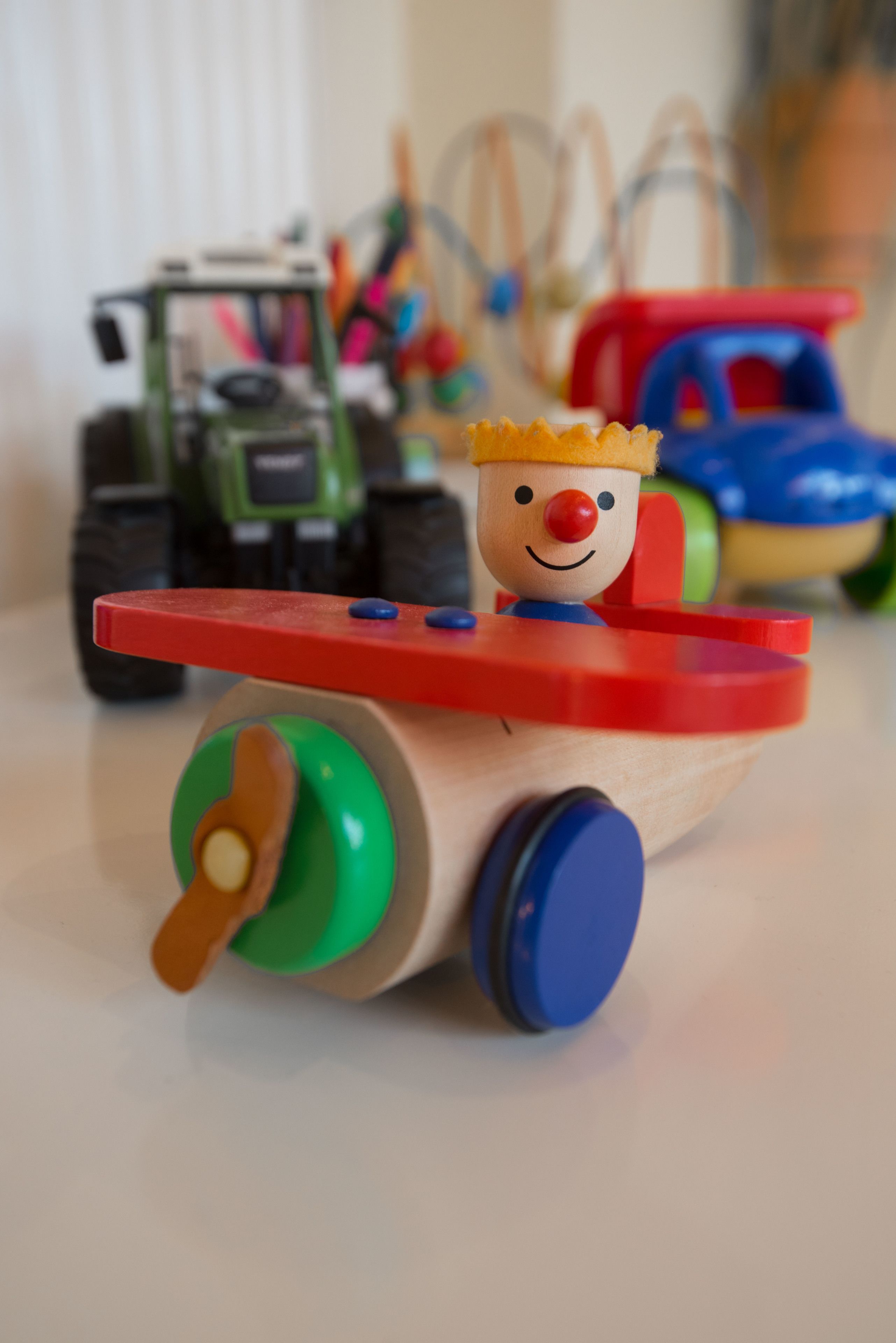 A toy airplane with a wooden body, red propeller, and a smiling face on top.