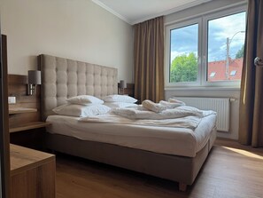A neatly made bed with white linens and towels, a wooden headboard, a bedside table with a lamp, and a window with curtains. - Der Marienhof Hotel Garni (Graz)