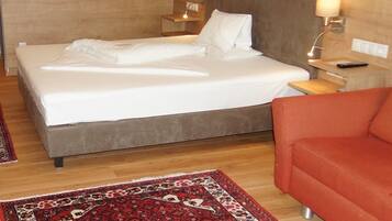 A hotel room with a large bed, two bedside tables with lamps, a red sofa, and a wall-mounted painting of deer antlers.