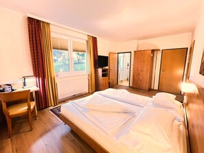 A hotel room with a bed, a desk, a chair, a TV, and a wardrobe.