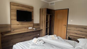 A bedroom with a wooden headboard, a flat-screen TV, a wardrobe, and a bed with neatly made white linens and towels.