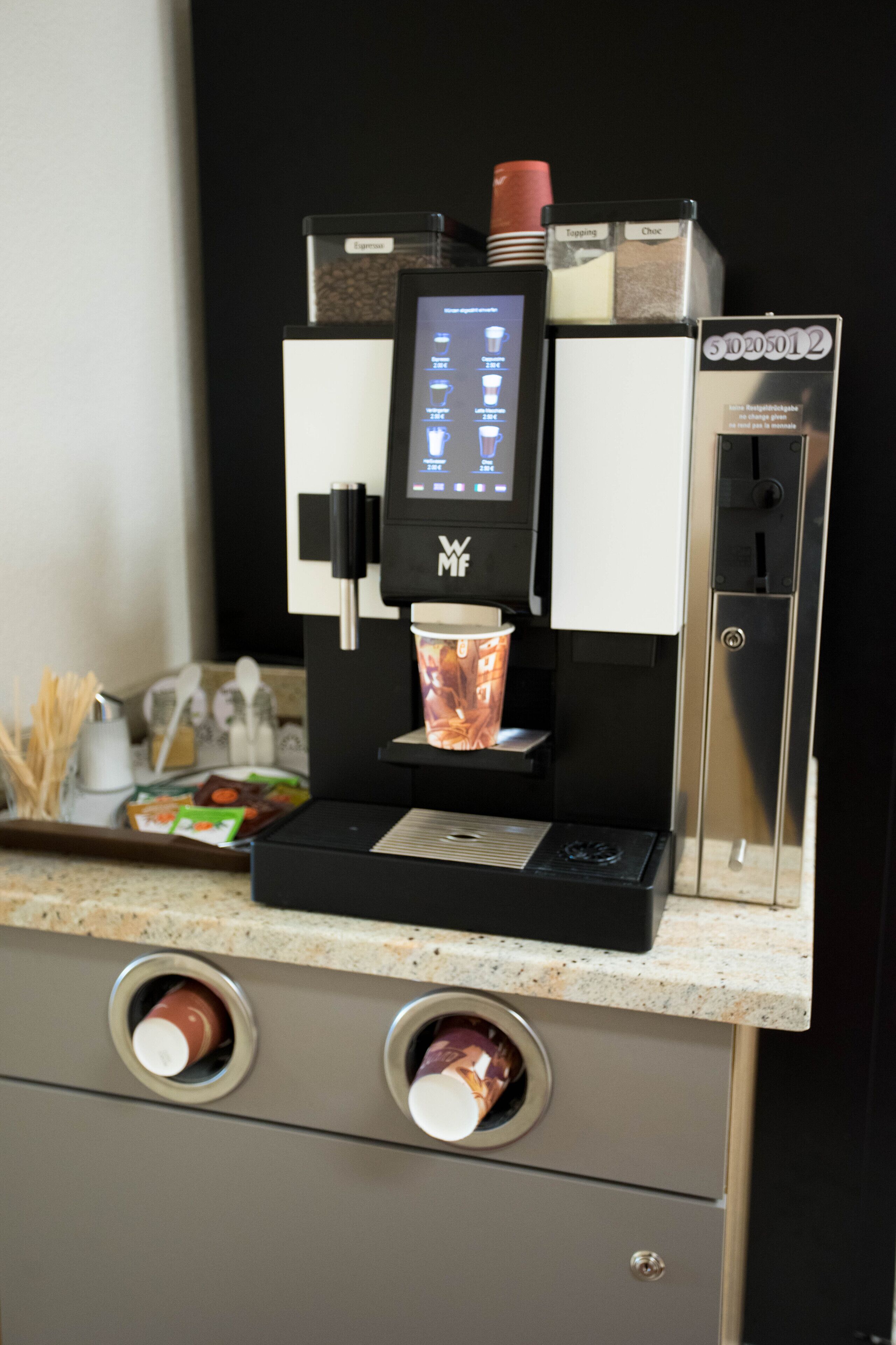 Une machine à café dotée d’un écran numérique, d’un porte-tasse et d’un petit plateau contenant des condiments.