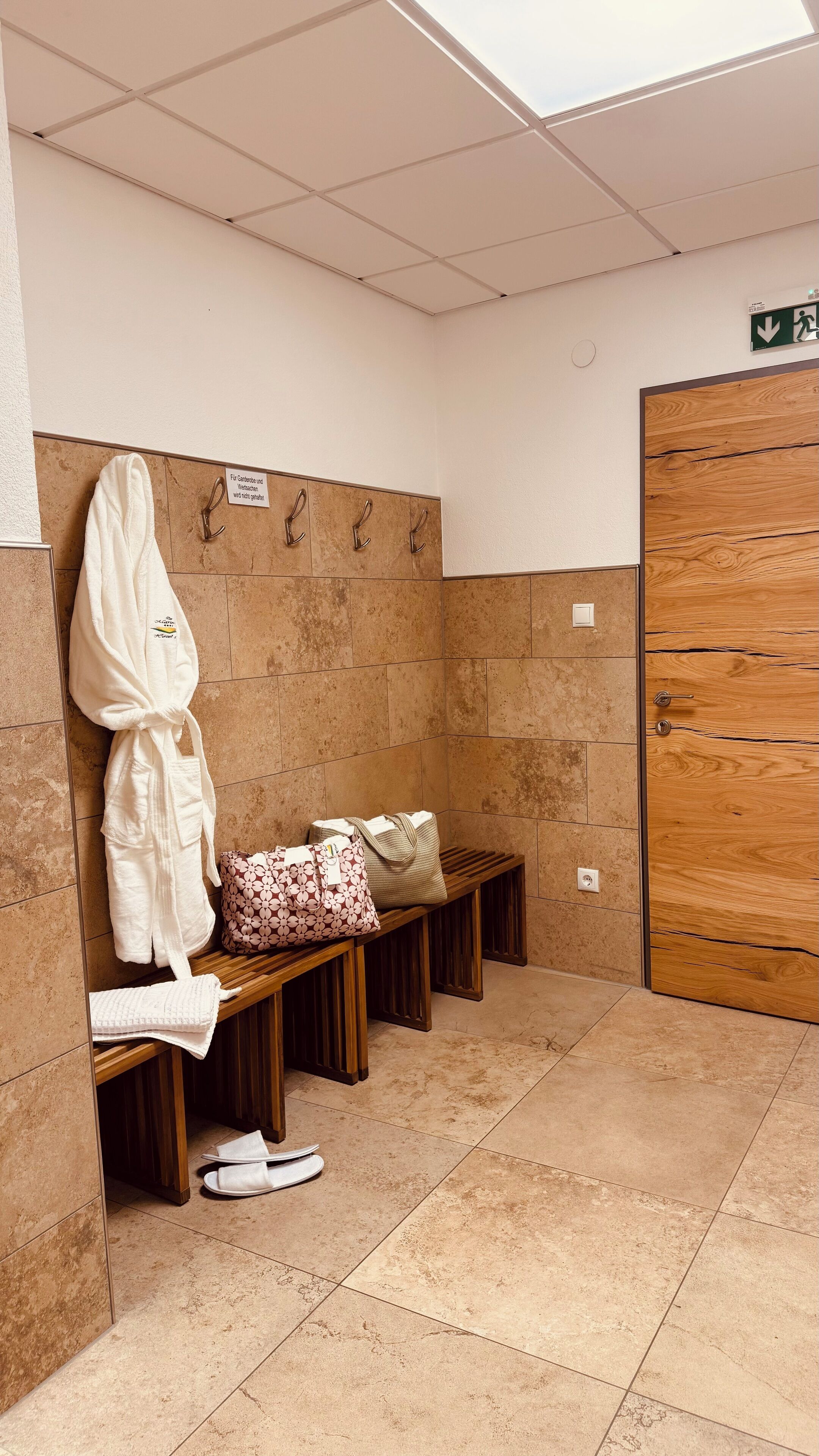 Ein Badezimmer mit einer Bank, einer Holztür und einem Handtuchhalter mit Bademänteln.