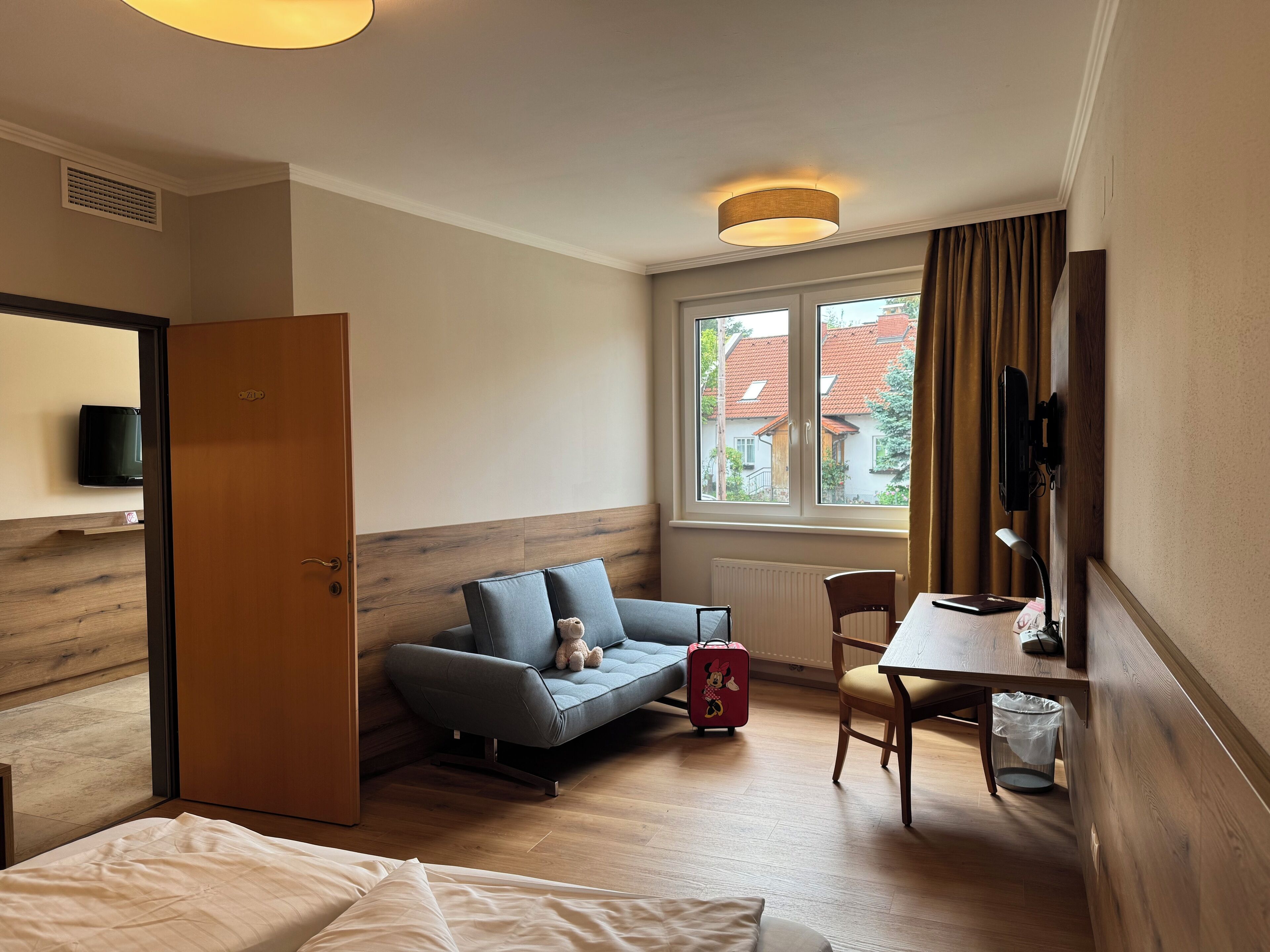 A hotel room with a bed, a sofa, a small table, a chair, a TV, and a window with curtains.