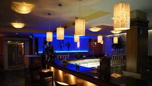 A bar area with wooden bar counter, hanging pendant lights, and a blue-lit wall. - Hotel Kufsteinerhof (Kufstein)