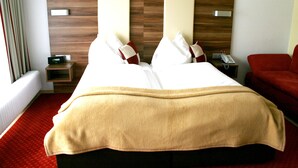 A hotel room with a large bed, a bedside table with a phone, and a red armchair. - Hotel Kufsteinerhof (Kufstein)