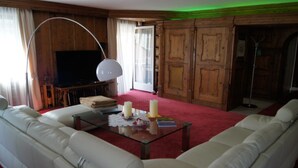 A living room with a large white sofa, a glass coffee table with candles, a television, and wooden paneling. - Hotel Kufsteinerhof (Kufstein)
