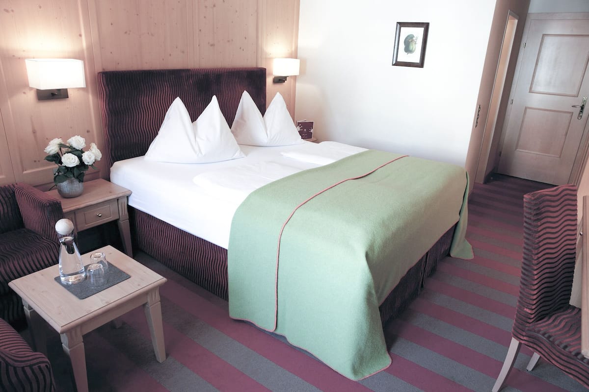 A hotel room with a bed, bedside tables, a chair, and a small table with a vase of flowers.