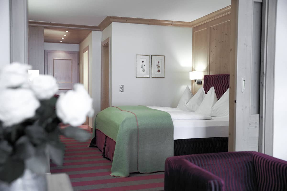 A hotel room with a bed, a chair, a bedside table, and a lamp.