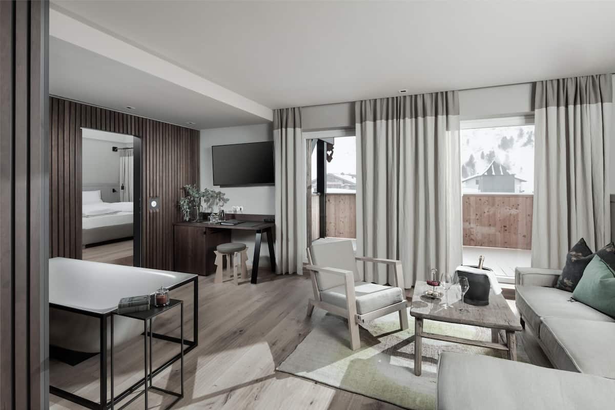 A modern living room with a sofa, a dining table, a kitchen area, and a large window with curtains.