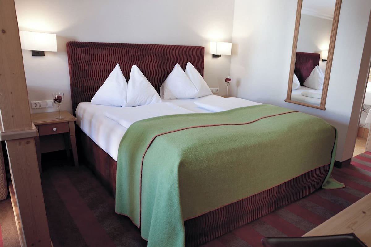 A hotel room with a bed, a nightstand, a mirror, and a red-striped carpet.