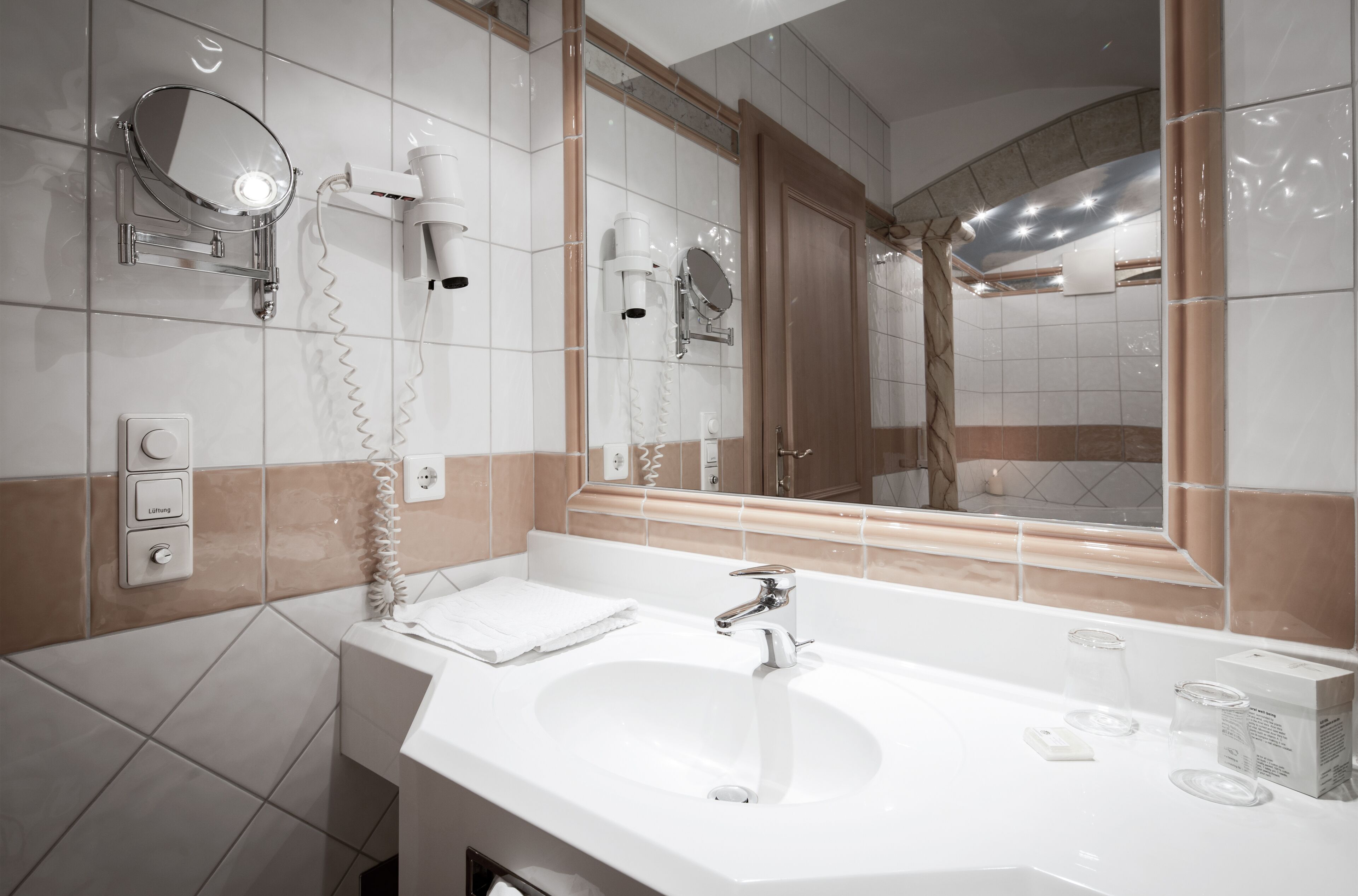 A modern bathroom with a large mirror, a sink, and a hairdryer mounted on the wall.