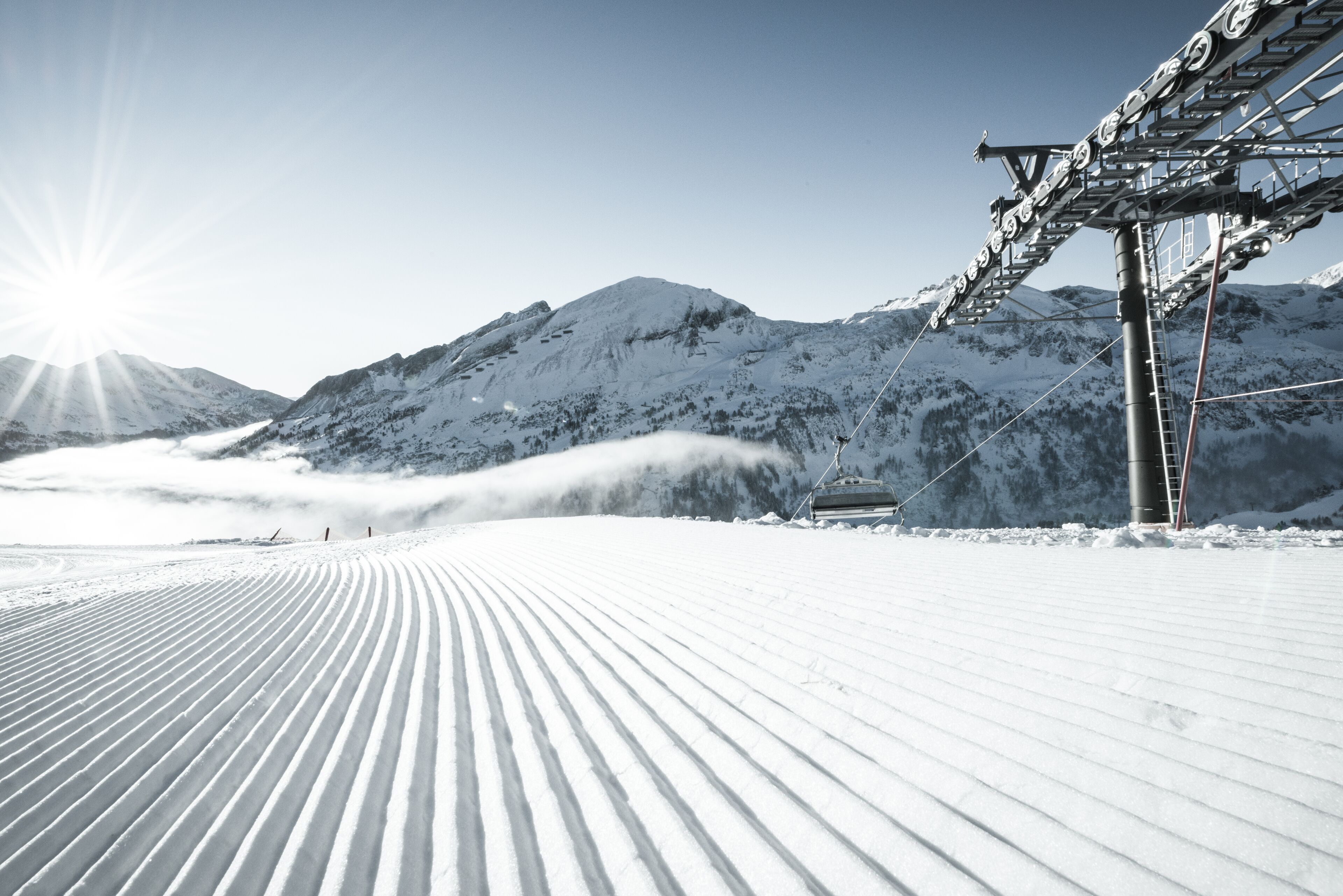 Pista de esquí nevada con un telesilla y montañas al fondo.