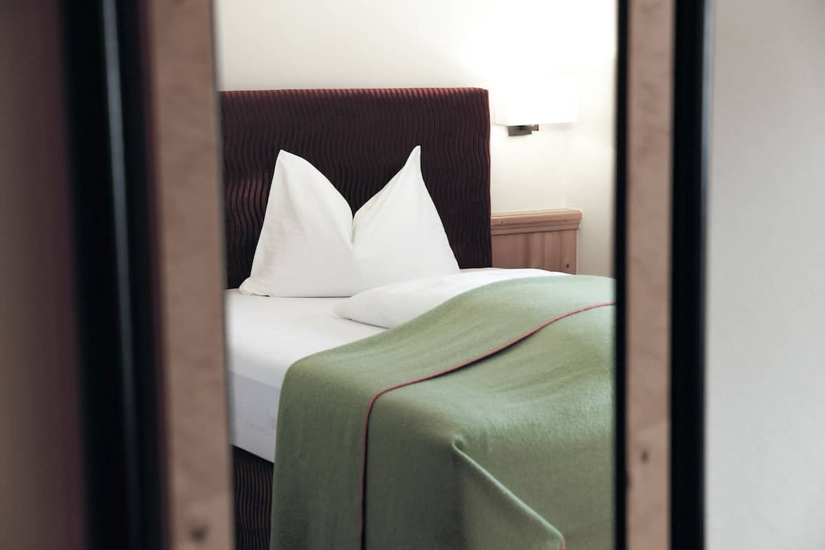 A neatly made bed with white pillows and a green bedspread, a wooden headboard, and a bedside lamp.