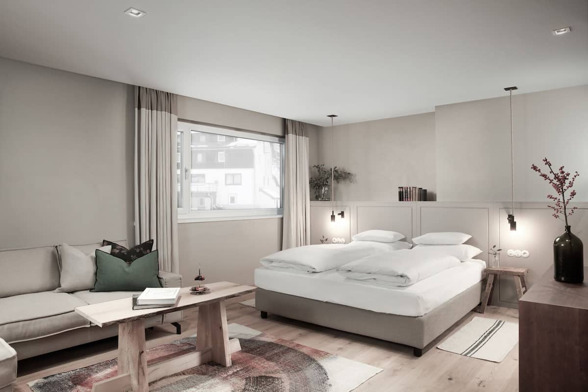 A modern hotel room with a bed, a sofa, a desk, and a large window.