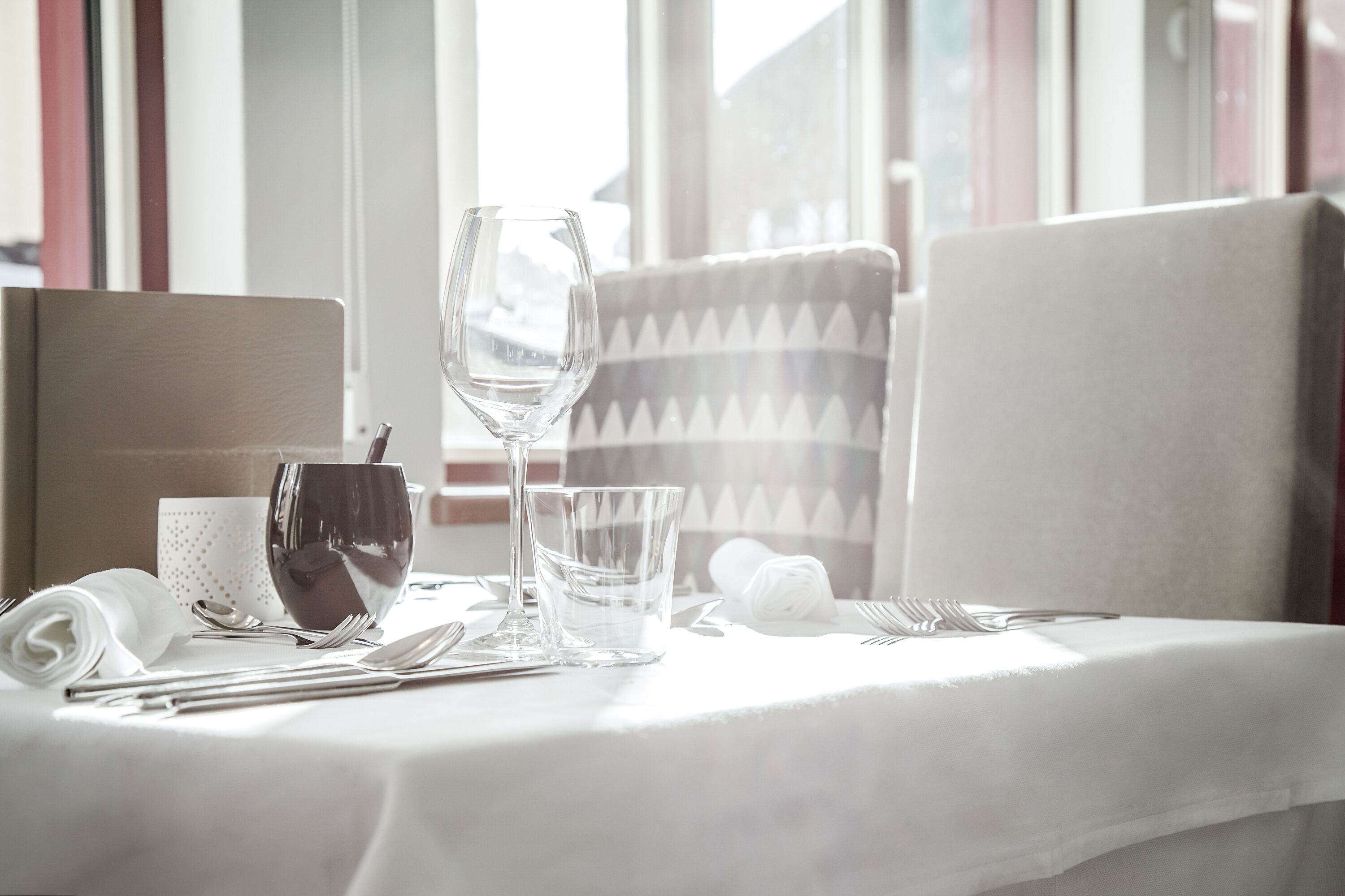 Une table à manger élégamment dressée, avec une nappe blanche, de la vaisselle transparente et une serviette pliée.