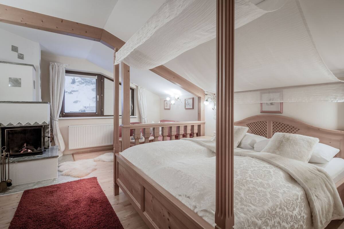 A four-poster bed with a wooden headboard, a fireplace, and a view of a snowy landscape through a window.