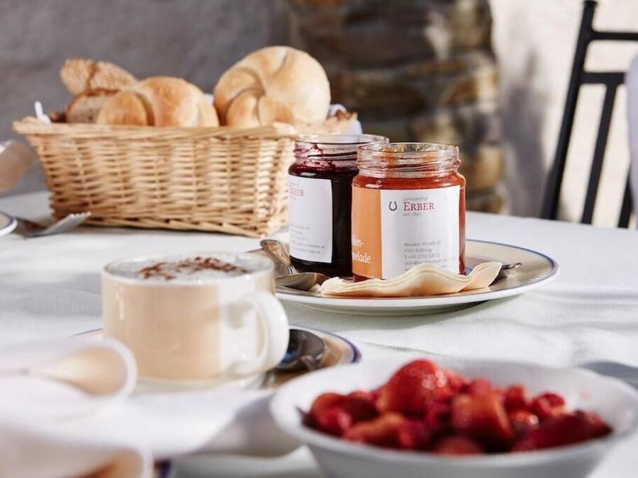 A breakfast setting with bread, jam, a cup of coffee, and a bowl of strawberries.