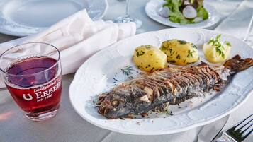 Ein Teller mit einem ganzen Fisch, Kartoffeln und einem Glas Rotwein.