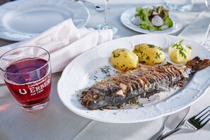 Ein Teller mit einem ganzen Fisch, Kartoffeln und einem Glas Rotwein.