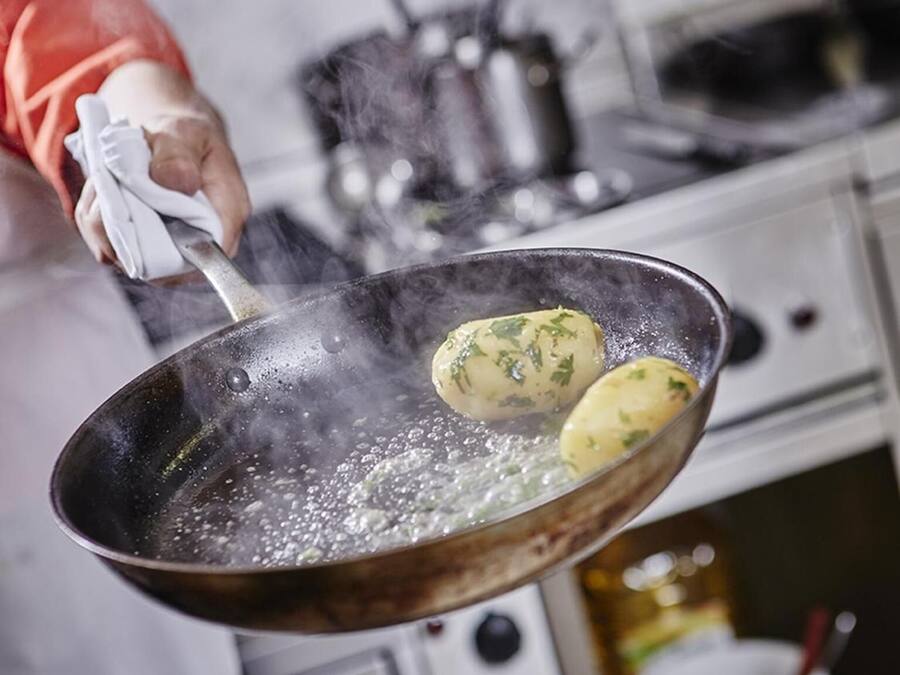 Una persona cucina patate in una padella sul fornello.