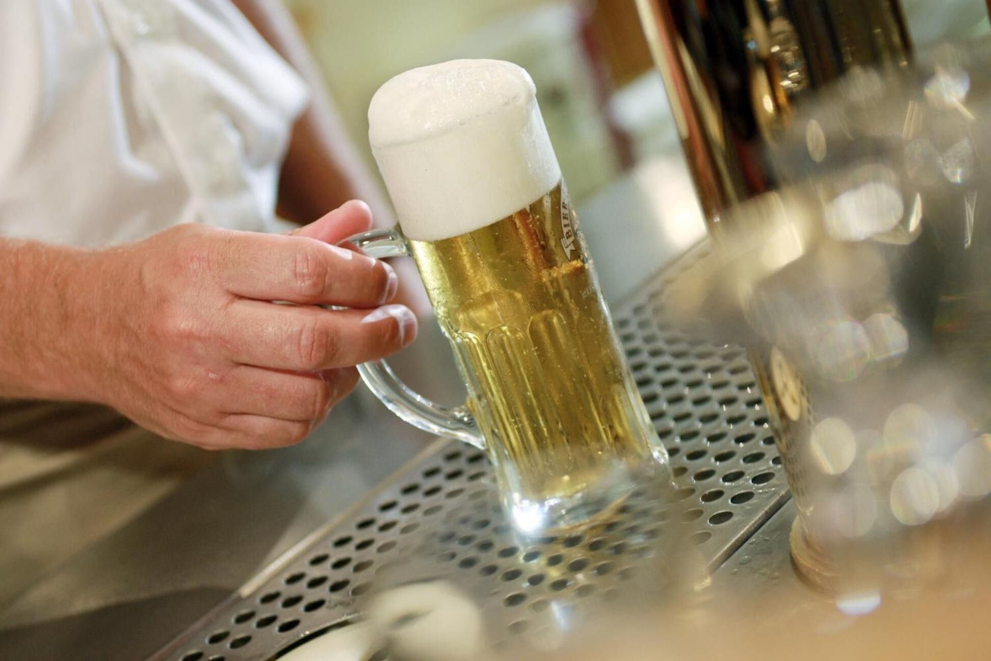 Eine Hand hält ein Bierglas auf einer Metallbar.