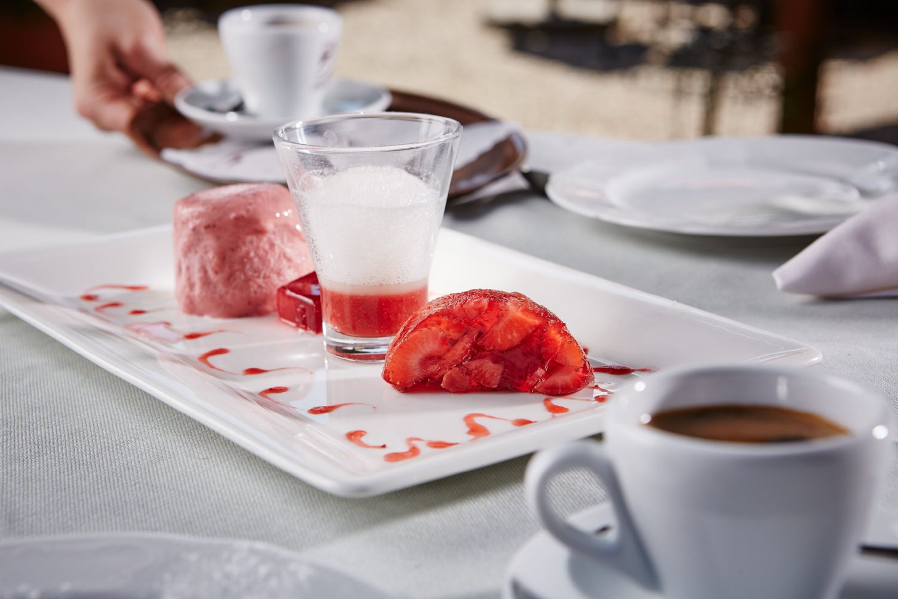En desserttallerken med is og frugtsalat, et glas rød drik og en kop kaffe.